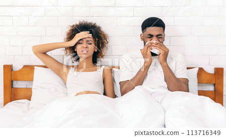 Sick african-american couple blowing noses in bed Sick african-american couple blowing noses in bed 113716349