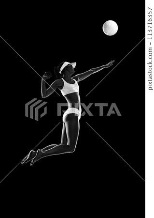 Athletic young woman, sportsman, beach volleyball player in mid-air hitting ball. against black background. Monochrome filter. 113716357