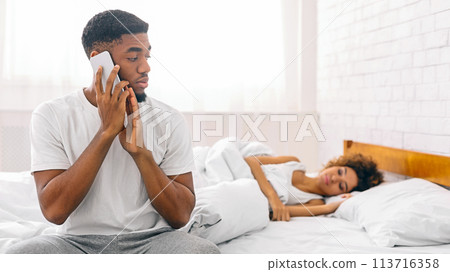 Man on call with woman sleeping beside Man on call with woman sleeping beside 113716358
