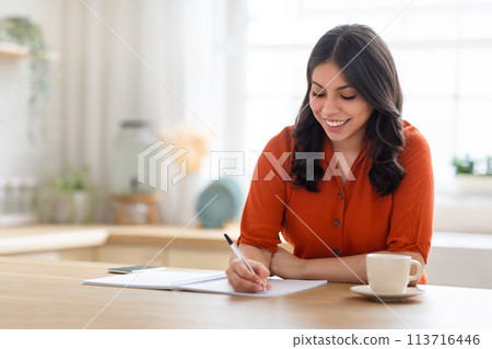 Happy woman writing in notebook at home 113716446