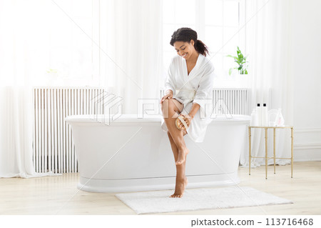 Joyful woman sitting on white bathtub, massaging her legs 113716468