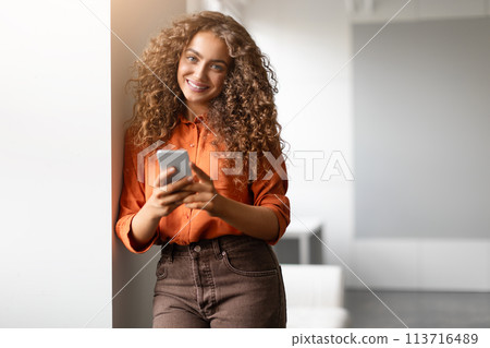 Woman with phone smiling in modern setting 113716489