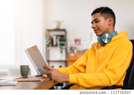 Man reading a book with headphones around neck at desk 113716507