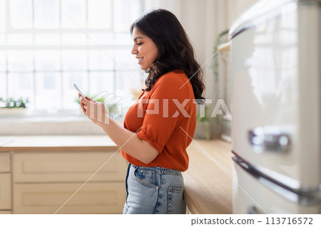 Woman using smartphone in a sunny kitchen 113716572