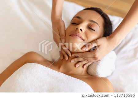 therapist rubbing relaxed woman's chin during facial massage at spa therapist rubbing relaxed woman's chin during facial massage at spa 113716580