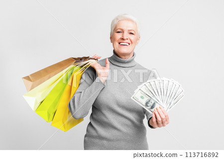 Elderly woman with money and bags on grey background Elderly woman with money and bags on grey background 113716892