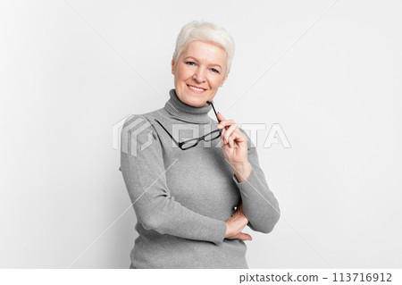 Senior woman with glasses, looking thoughtful on grey background 113716912