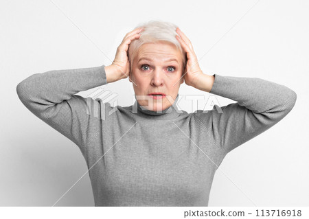 Elderly woman holding head in surprise on grey background Elderly woman holding head in surprise on grey background 113716918