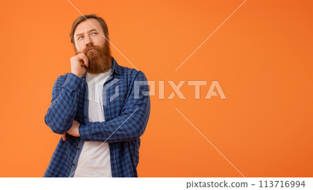 Thoughtful redhaired bearded businessman in casual thinking against orange background Thoughtful redhaired bearded businessman in casual thinking against orange background 113716994
