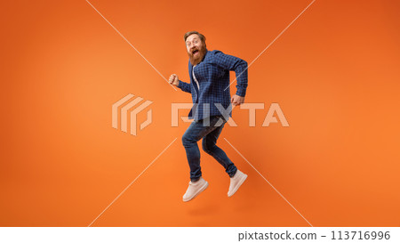 Excited redhaired bearded guy jumping and shouting over orange backdrop 113716996