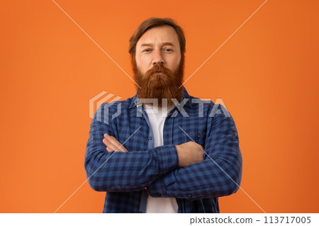 Redhaired bearded man crossing arms on chest against orange backdrop Redhaired bearded man crossing arms on chest against orange backdrop 113717005