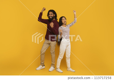 Man and woman with fists pumped on yellow background 113717258
