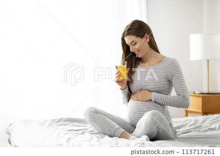 Pregnant woman enjoying a glass of juice on bed Pregnant woman enjoying a glass of juice on bed 113717261
