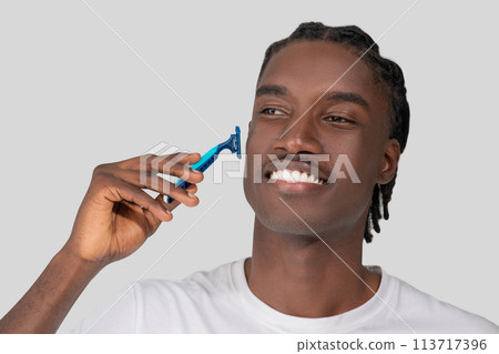 Man shaving with a blue razor on white background 113717396
