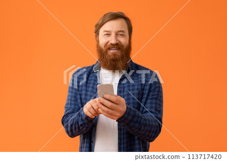 Man with red hair and beard engages with smartphone, studio 113717420