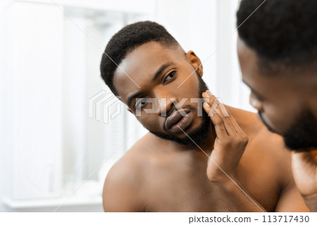 Man applying cream on face in front of bathroom mirror Man applying cream on face in front of bathroom mirror 113717430