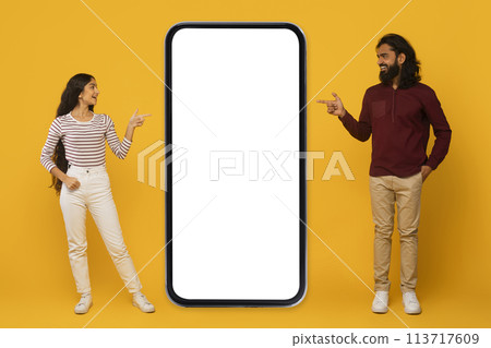 Man and woman pointing at blank phone screen on yellow 113717609