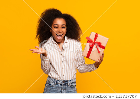 Excited woman holding a gift box on yellow background Excited woman holding a gift box on yellow background 113717707