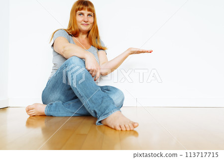 Full length portrait gorgeous cheerful woman sitting on parquet floor, empty space an apartment without furniture 113717715