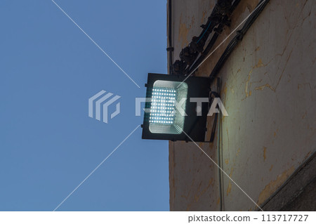 An LED lantern mounted on the street wall dimly illuminates the wall during dusk on dark blue sky background. The interval of time of day that is observed by a change in the degree of illumination An LED lantern mounted on the street wall dimly illuminates the wall during dusk on dark blue sky background. The interval of time of day that is observed by a change in the degree of illumination 113717727