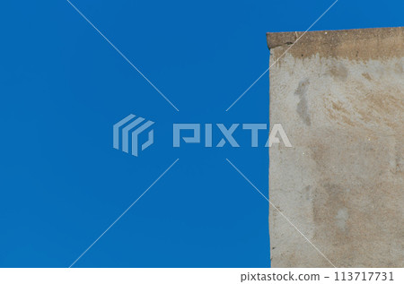 A small section of the edge of a blurred building wall with rough uneven plaster against a blue clear sky. Blank for artwork, mockup A small section of the edge of a blurred building wall with rough uneven plaster against a blue clear sky. Blank for artwork, mockup 113717731