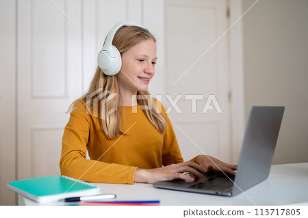 Teen Girl Using Laptop And Headphones at Desk 113717805