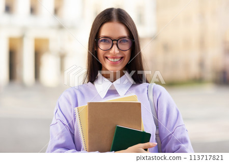 Smiling student holding books in urban setting Smiling student holding books in urban setting 113717821