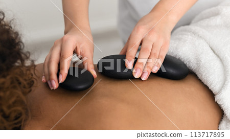 Masseur placing stone on back of woman 113717895