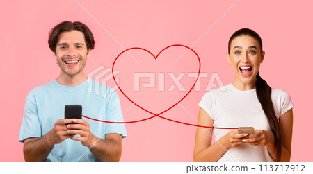 A man in a blue shirt happily using his smartphone and a woman in a white tee, with her hair in a ponytail 113717912