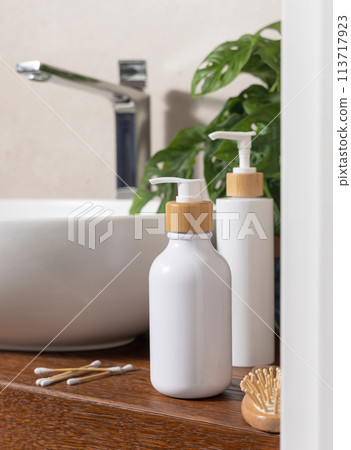 White cosmetic bottles near basin and green plant on wooden countertop in bath, mockup White cosmetic bottles near basin and green plant on wooden countertop in bath, mockup 113717923