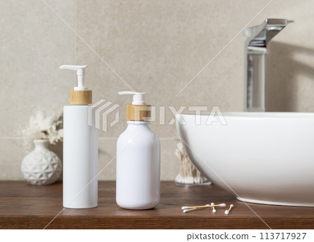 Cosmetic bottles near basin on wooden countertop in bath, mockup 113717927