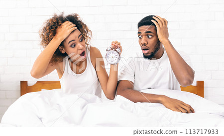 Confused couple missed ringing of alarm clock in bed Confused couple missed ringing of alarm clock in bed 113717933