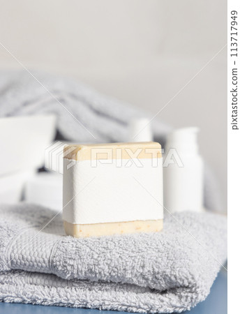 Soap bar with blank label on light grey towel near basin and cream bottles in bath, mockup 113717949