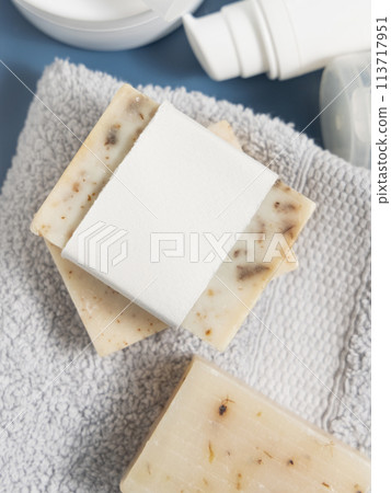 Soap bar with blank label on light grey towel near cream bottles on blue, mockup Soap bar with blank label on light grey towel near cream bottles on blue, mockup 113717951