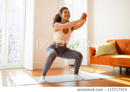 lady athlete performs squats and stretches her arms forward indoor 113717954