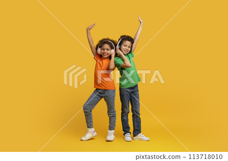 Siblings dancing with raised arms on yellow background Siblings dancing with raised arms on yellow background 113718010