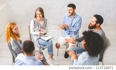 Friendly therapy group members applauding to young woman's progress in rehabilitation 113718071
