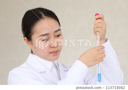 A woman in a white coat conducting an experiment with a serious expression while holding a test tube 113718082
