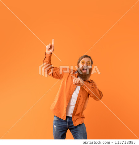 Energetic redhaired man pointing upward with joy while dancing, studio 113718083