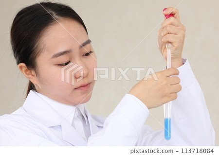A woman in a white coat conducting an experiment with a serious expression while holding a test tube A woman in a white coat conducting an experiment with a serious expression while holding a test tube 113718084