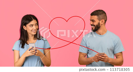 A young woman with a gentle smile, holding a smartphone, glances at a bearded man also with a phone A young woman with a gentle smile, holding a smartphone, glances at a bearded man also with a phone 113718305