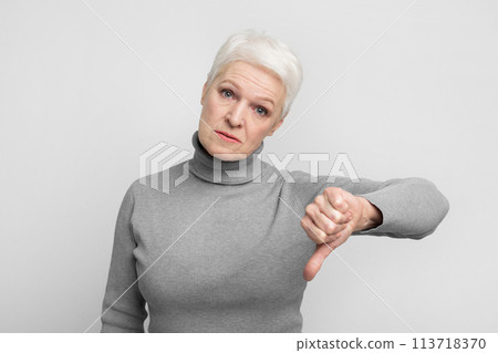 Senior woman giving thumbs down with displeasure Senior woman giving thumbs down with displeasure 113718370