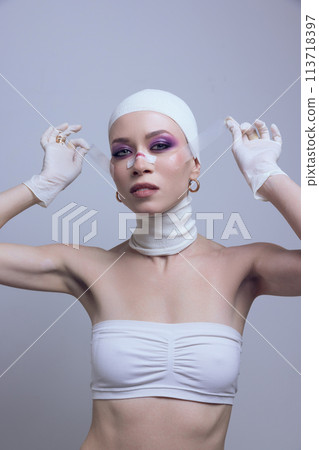 Woman with striking makeup unveiling bandage from face after plastic surgery on pastel purple background. Futuristic skincare line 113718397