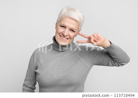 Playful senior woman with peace sign near eye Playful senior woman with peace sign near eye 113718494