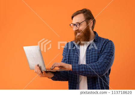 Middle aged redhaired guy with beard using laptop in studio Middle aged redhaired guy with beard using laptop in studio 113718620