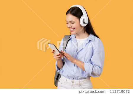 Woman focused on smartphone with headphones, yellow background 113719072