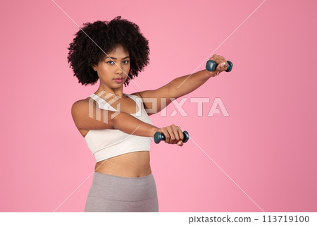 Sporty African American lady lifting weights on pink background 113719100