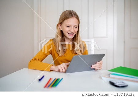 Cheeful Teen Girl Sitting at Table With Tablet Cheeful Teen Girl Sitting at Table With Tablet 113719122