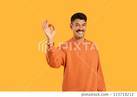 Joyful guy making OK gesture on orange 113719212