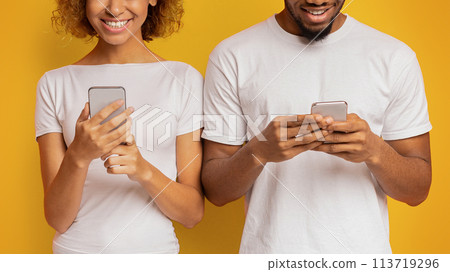 Cheerful black millennial couple browsing on cellphones 113719296